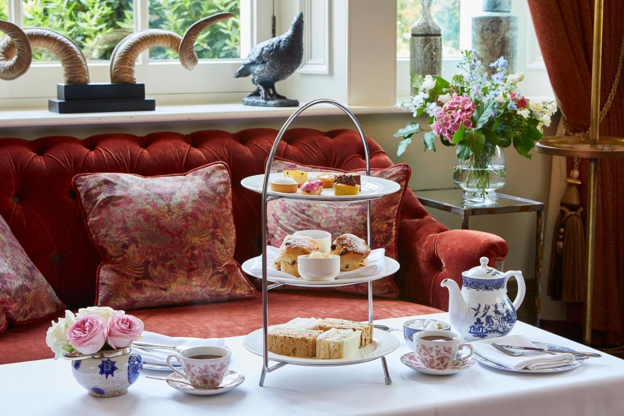 Macdonald Bath Spa Hotel Exterior foto The photo showcases an elegant afternoon tea setting. In the foreground, there is a three-tiered serving stand filled with various pastries and scones, including some topped with cream and fruit. Surrounding the stand is a beautifully arranged table 