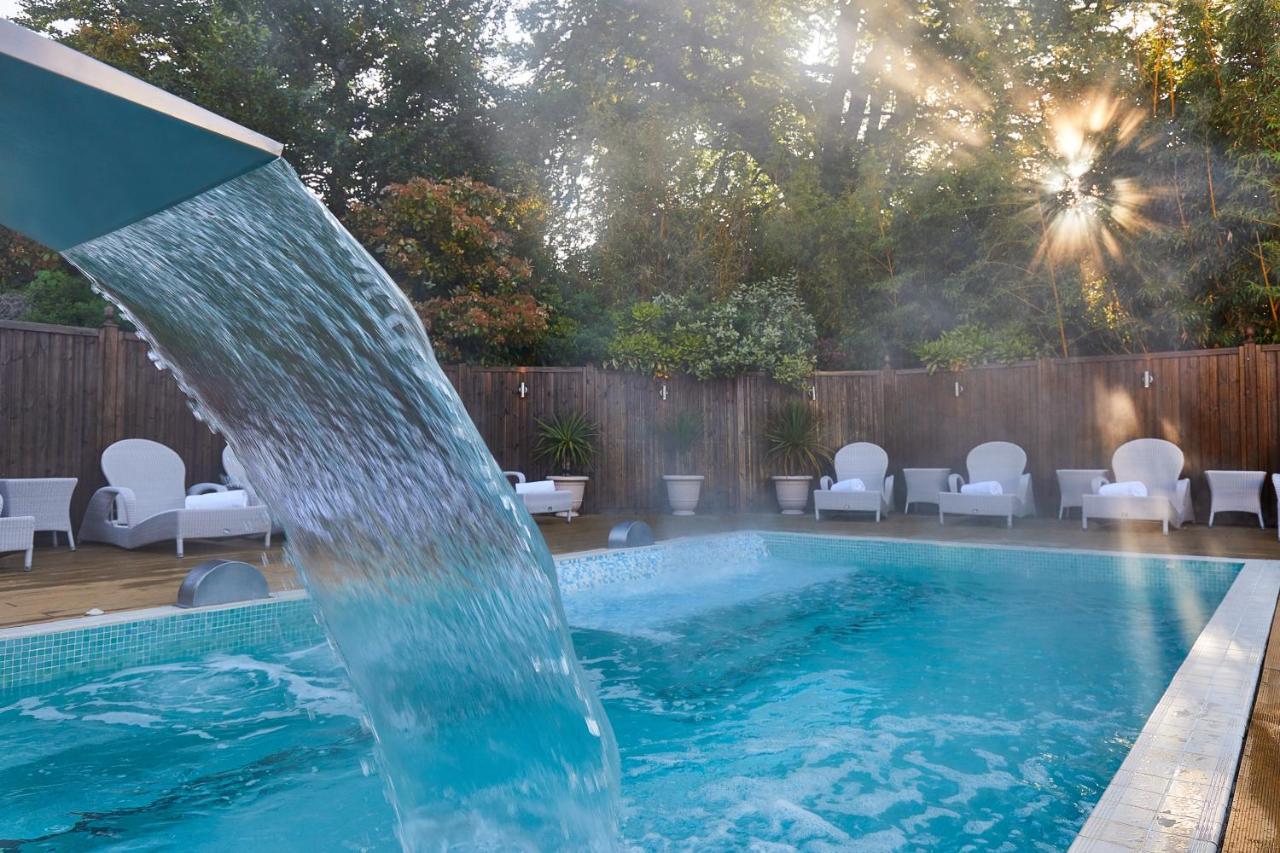 Macdonald Bath Spa Hotel Exterior foto The photo shows a tranquil swimming pool surrounded by greenery. Water is cascading from a feature into the pool, creating a refreshing effect. In the background, there are white lounge chairs positioned neatly along the poolside, inviting relaxation