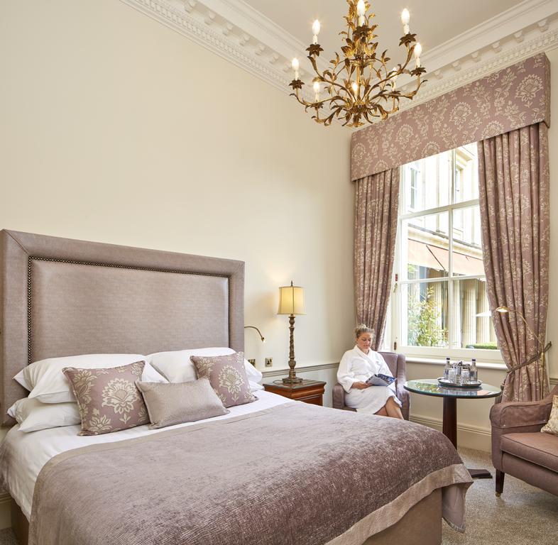 Macdonald Bath Spa Hotel Exterior foto The photo shows a well-appointed hotel room that features a large, elegant bed with soft bedding and decorative pillows. The walls are painted a light color, and there is an ornate chandelier hanging from the ceiling. A beautiful window is adorned wi