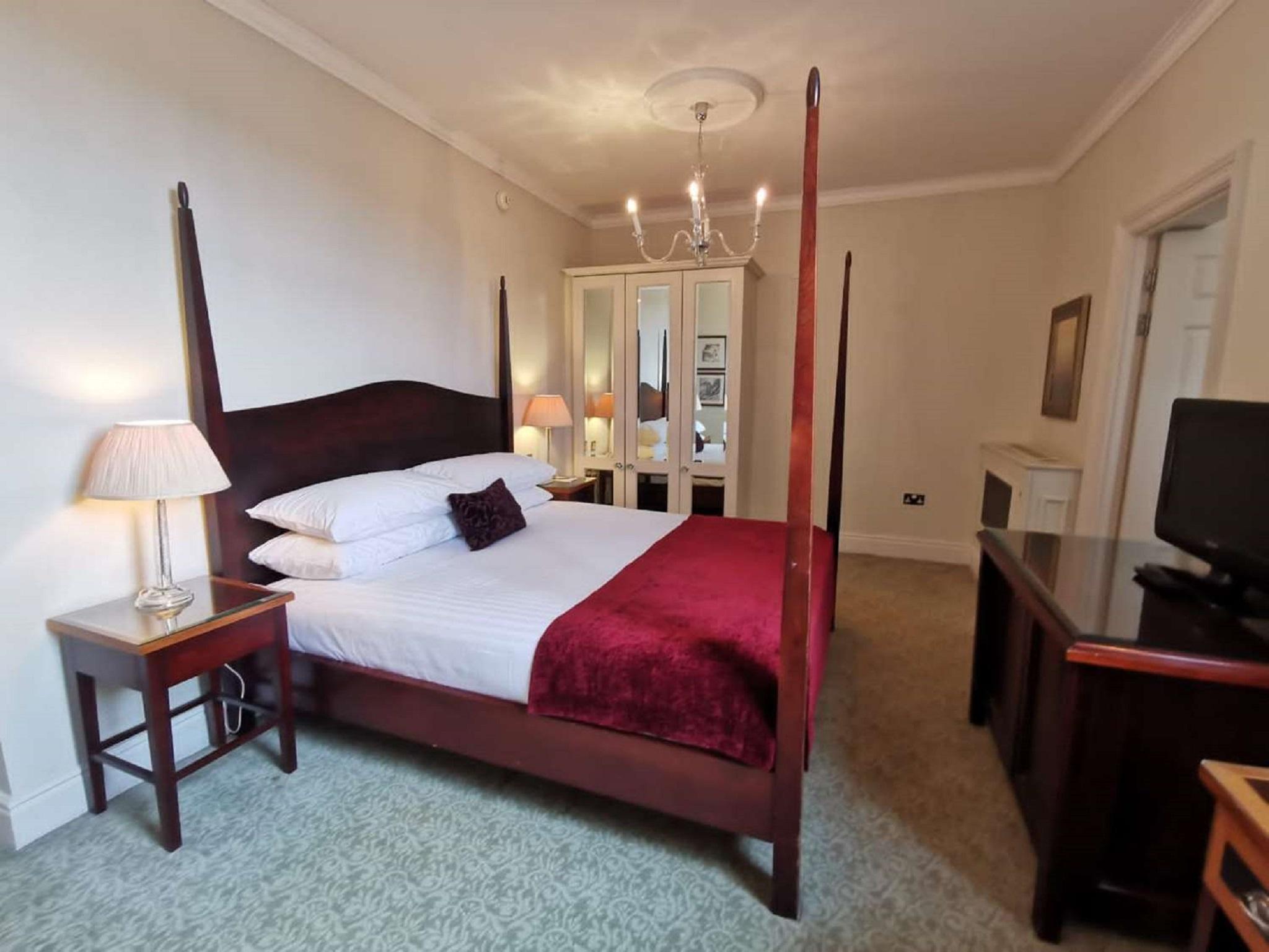 Macdonald Bath Spa Hotel Exterior foto The photo shows a well-decorated bedroom featuring a four-poster bed with white pillows and a burgundy throw. There are two bedside lamps on wooden nightstands on either side of the bed. A large wardrobe or mirror cabinet is visible in the background