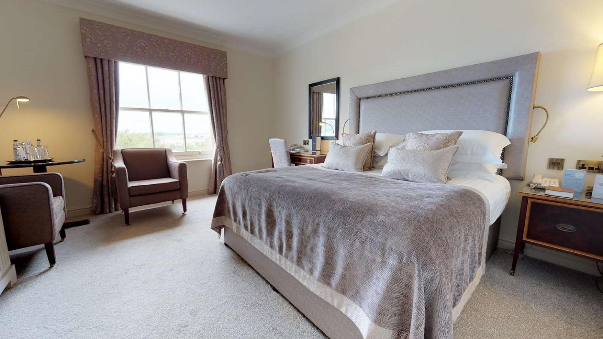 Macdonald Bath Spa Hotel Exterior foto The photo shows a well-furnished bedroom. It features a large bed with a light gray headboard and several decorative pillows on top. The bed is covered with a soft gray blanket. To one side of the room, there is a comfortable armchair and a small tab