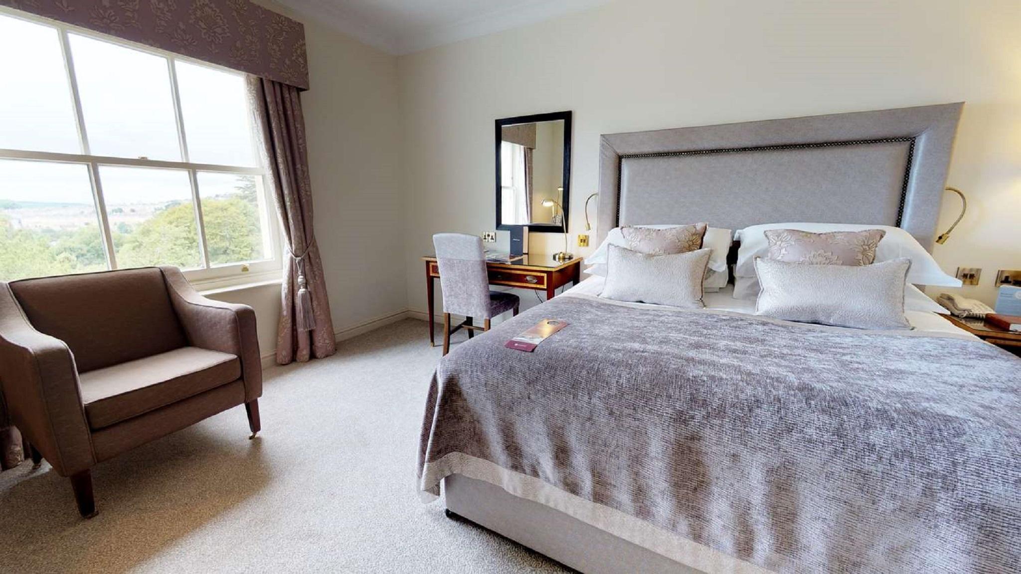 Macdonald Bath Spa Hotel Exterior foto The photo shows a cozy and well-decorated bedroom. It features a large bed with a plush, grey bedspread and several decorative pillows. Beside the bed, there is a wooden bedside table with a lamp. A small desk and chair are positioned near a window, 