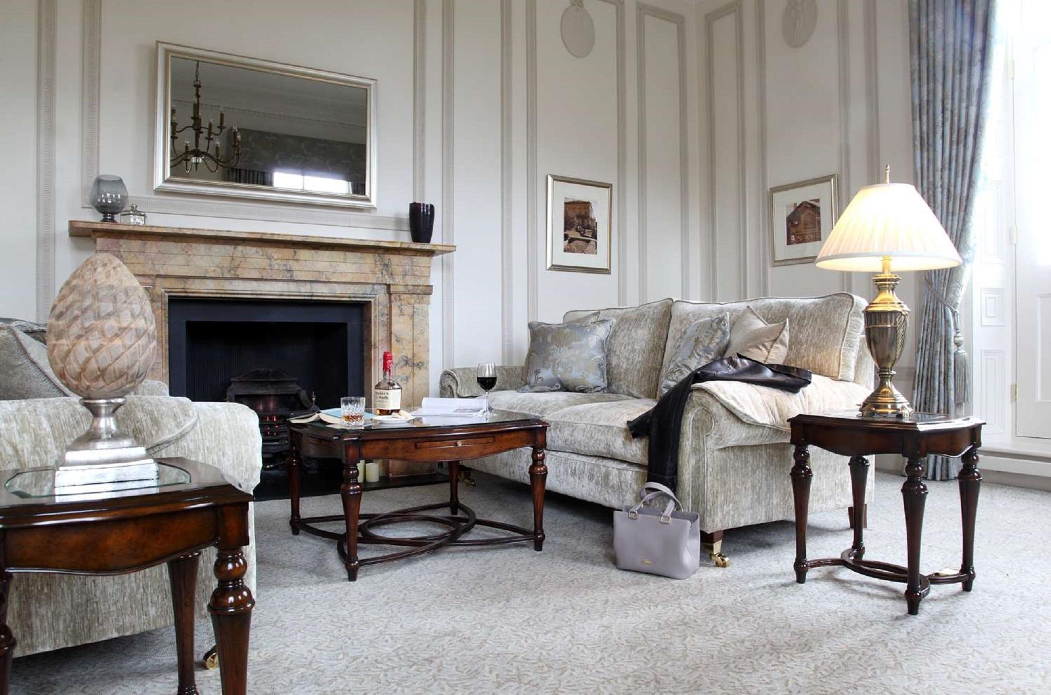 Macdonald Bath Spa Hotel Exterior foto The photo shows a stylish living room. It features a plush light-colored sofa adorned with decorative pillows. Next to the sofa, there is a small wooden coffee table with a decorative item and a bottle of wine, along with a glass. A larger wooden tab