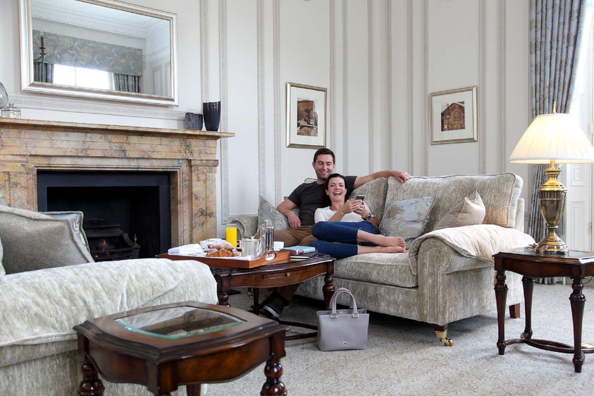 Macdonald Bath Spa Hotel Exterior foto The photo shows a cozy living room setting where a couple is sitting together on a light-colored sofa. They appear relaxed, with the man sitting slightly behind the woman, who is smiling and looking at her phone. The room features elegant decor, incl