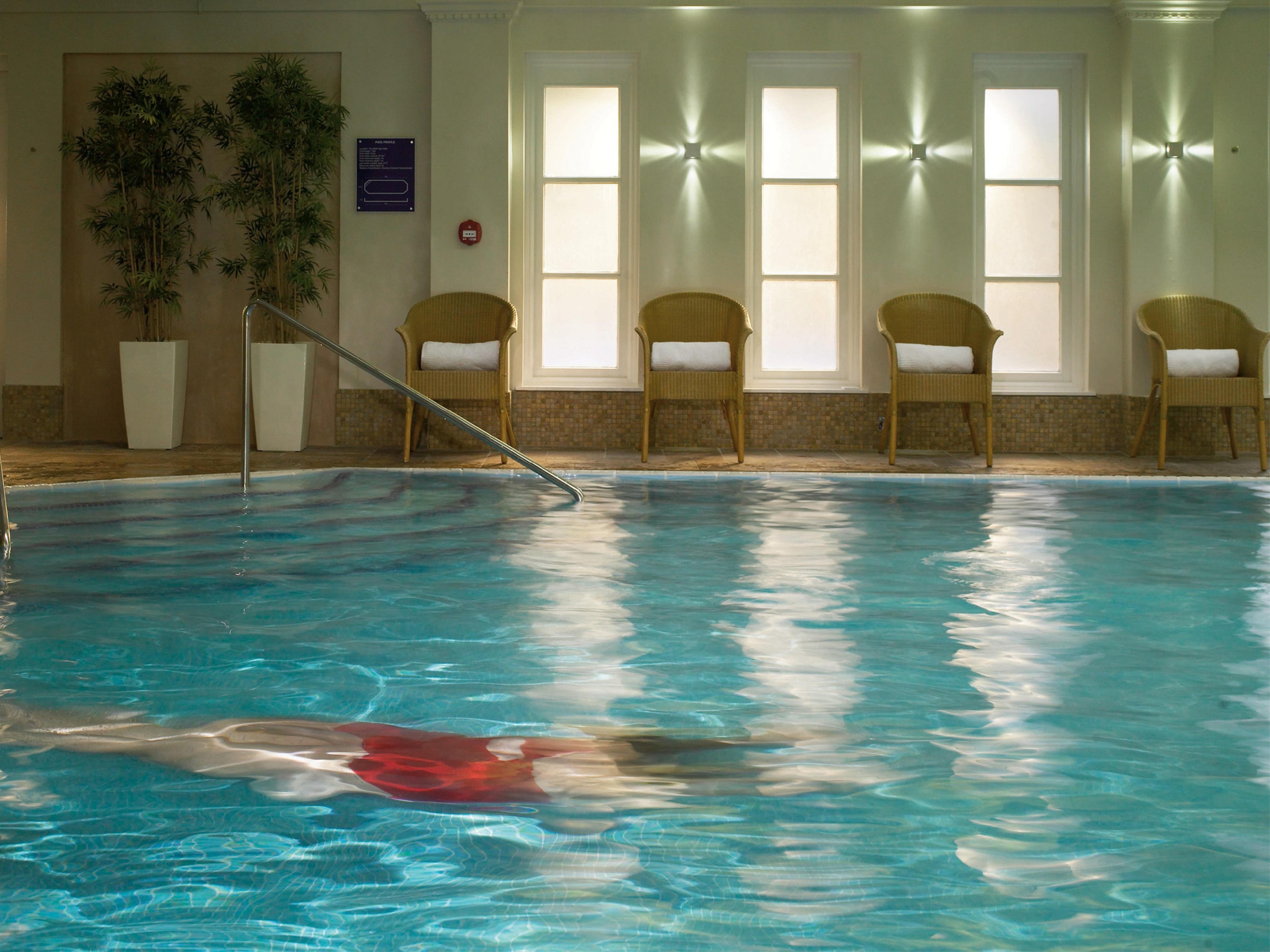 Macdonald Bath Spa Hotel Exterior foto The photo shows an indoor swimming pool with clear, blue water. In the pool, a person is swimming, partially submerged, and wearing a red swimsuit. Surrounding the pool, there are several empty chairs arranged along the side, along with potted plants