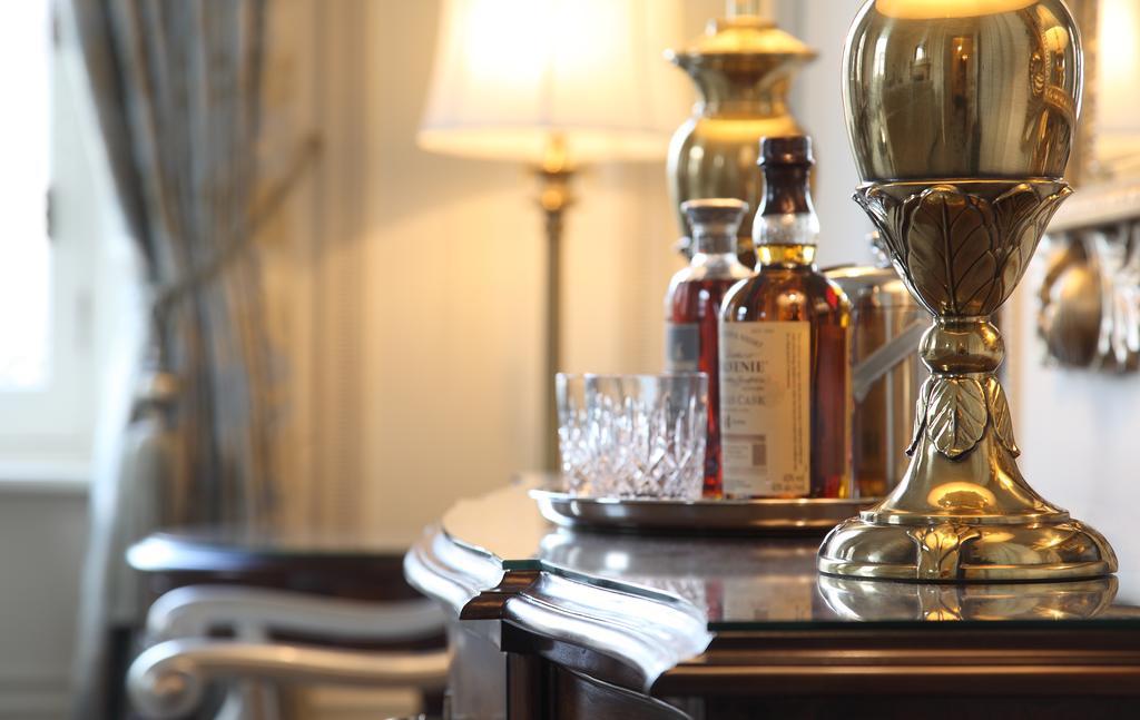 Macdonald Bath Spa Hotel Exterior foto The photo features an elegant interior scene that includes a polished wooden bar or table. On the surface, there are several bottles of liquor, likely whiskey, each with a distinctive label. A glass, possibly for drinking, is positioned near the bott