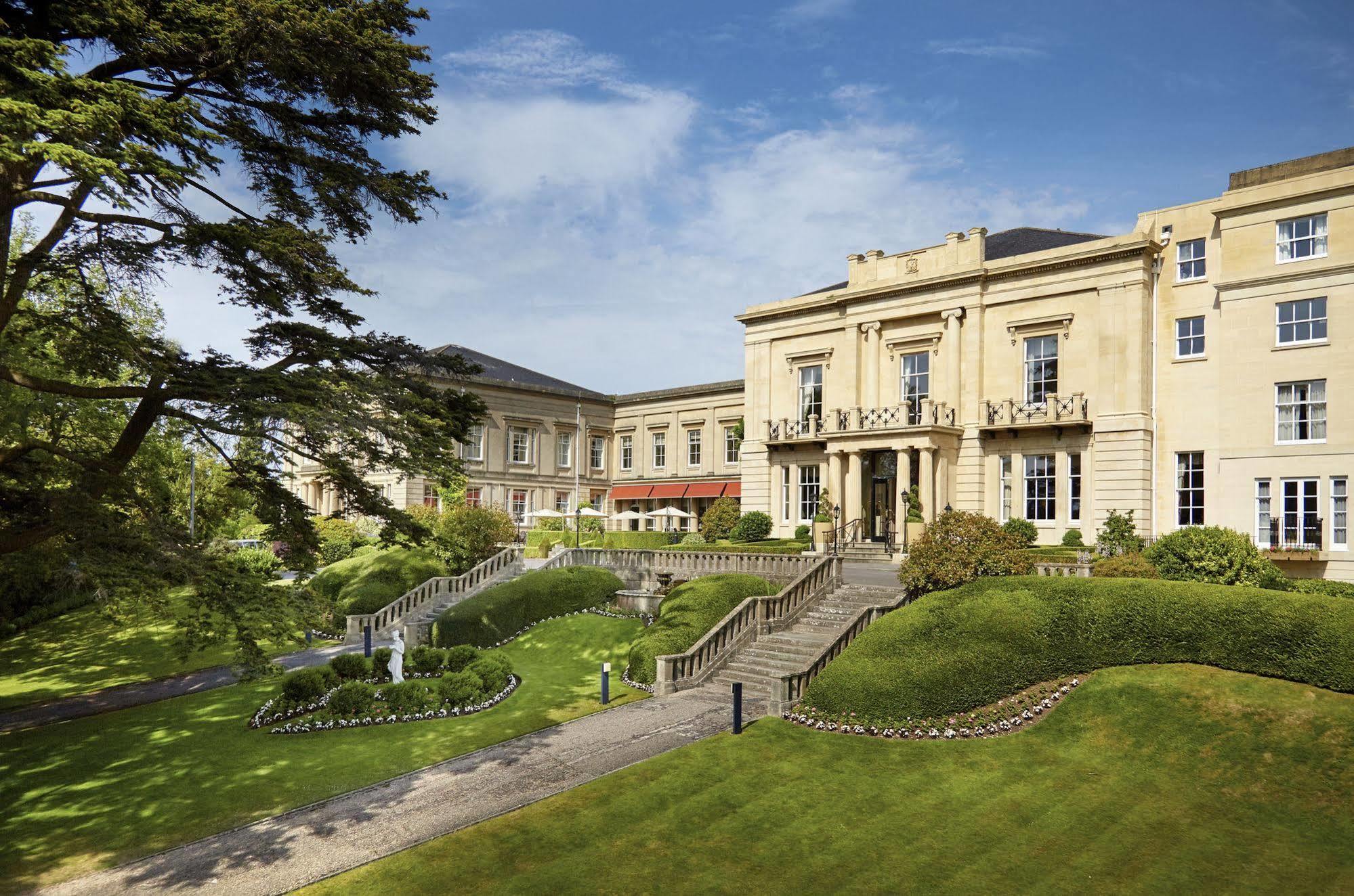 Macdonald Bath Spa Hotel Exterior foto The photo shows a grand building, likely a hotel or estate, surrounded by well-manicured gardens and lawns. The architecture appears elegant, with multiple stories and large windows. There are steps leading up to the entrance, and the setting include